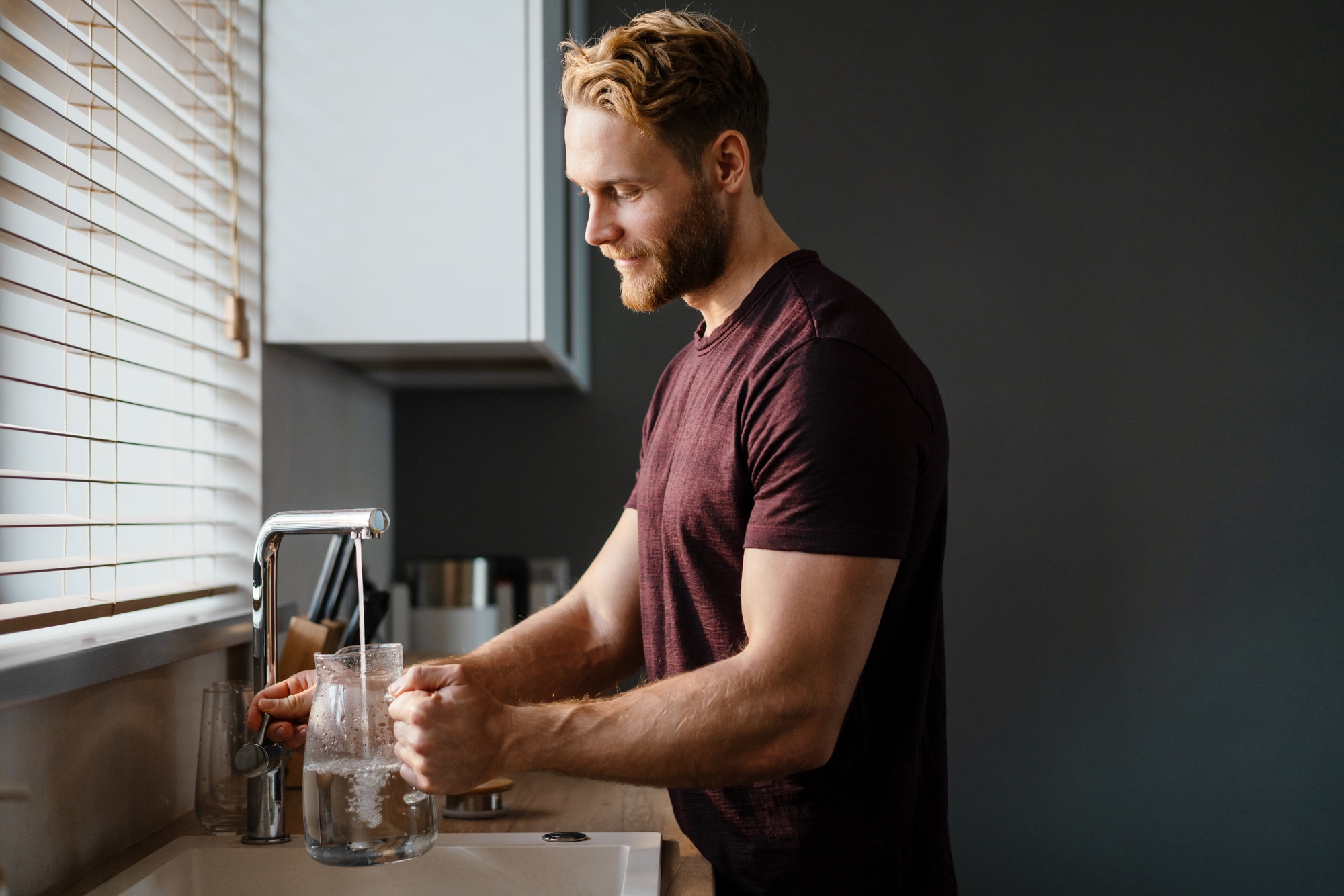 Smiling man pouring water in the jug from a tap